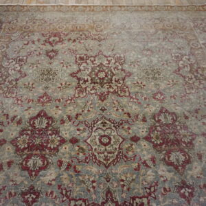 A distressed traditional rug featuring a burgundy and tan floral pattern on a faded blue-gray field.