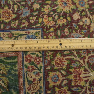 Close-up of a rug with a maroon field, floral patterns in yellow, green, and blue, and a visible ruler.