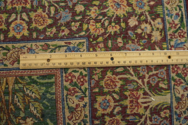 Close-up of a rug with a maroon field, floral patterns in yellow, green, and blue, and a visible ruler.