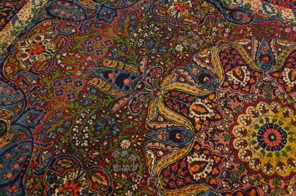 Detailed view of a low-pile rug featuring complex red, blue, green, and gold botanical and curvilinear designs.