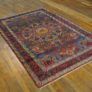 Jewel-toned rug with red, blue, and gold floral patterns lies on worn wide-plank wood flooring.