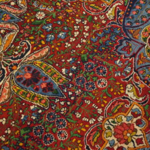 Detailed view of a low-pile rug with dense red, blue, yellow, and white floral and paisley motifs.