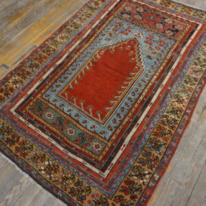 Low-pile rug with a detailed red field, blue arch, and multi-colored geometric borders resting on distressed hardwood.