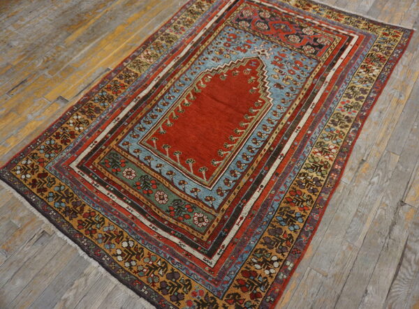 Low-pile rug with a detailed red field, blue arch, and multi-colored geometric borders resting on distressed hardwood.