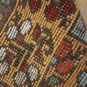 Multicolor low-pile geometric rug in brown, yellow, red, and white fibers rests against wood plank flooring.