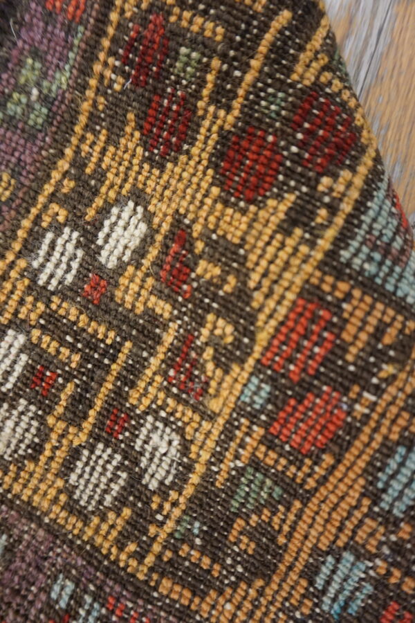 Multicolor low-pile geometric rug in brown, yellow, red, and white fibers rests against wood plank flooring.