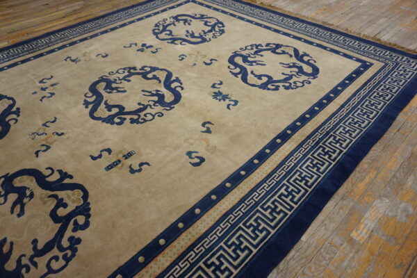 Low-pile beige rug with dark blue stylized dragon patterns and a geometric border on distressed wood.