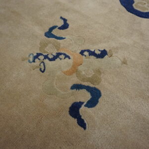 Detail of a plush beige rug with stylized blue, orange, and sage scrollwork motifs.