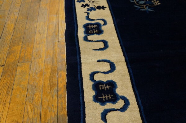 A close-up shows the navy rug border, featuring beige and blue winding motifs, next to distressed hardwood planks.
