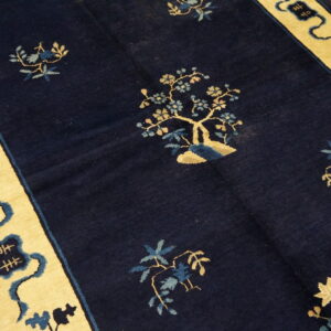 Navy rug with sparse gold and blue botanical pattern and wide yellow border featuring dark blue symbols on wood floor.