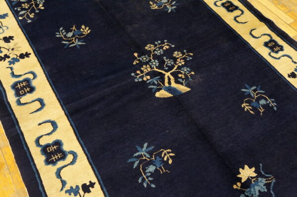 Navy rug with sparse gold and blue botanical pattern and wide yellow border featuring dark blue symbols on wood floor.