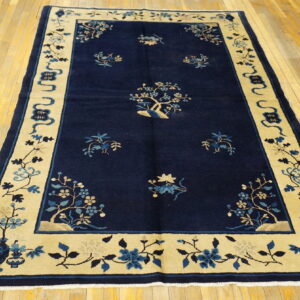 Deep blue rug with a contrasting wide light tan border displaying stylized blue floral motifs on a wood floor.