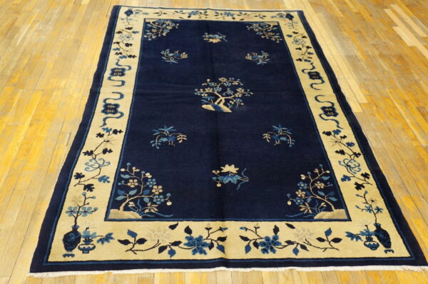 Deep blue rug with a contrasting wide light tan border displaying stylized blue floral motifs on a wood floor.