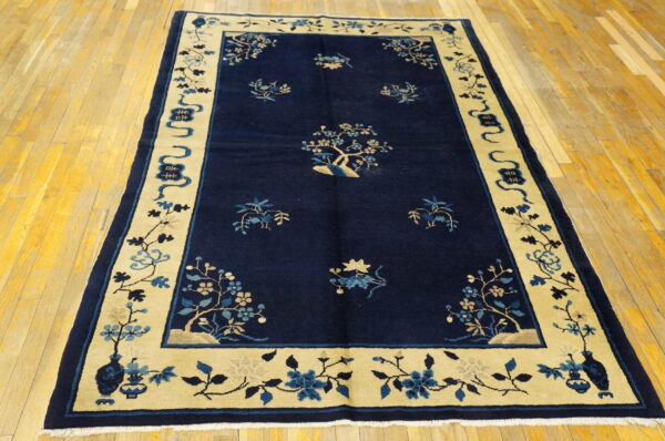 Navy blue rug with a wide tan border displaying blue floral designs on yellow wood planks.