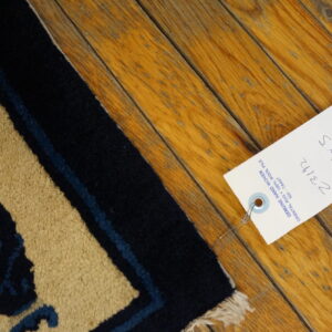 High pile tan rug featuring a navy and blue pattern rests on distressed warm-toned wood plank flooring.