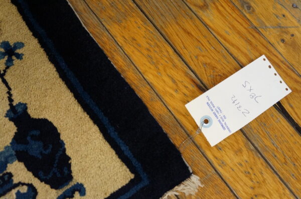 High pile tan rug featuring a navy and blue pattern rests on distressed warm-toned wood plank flooring.