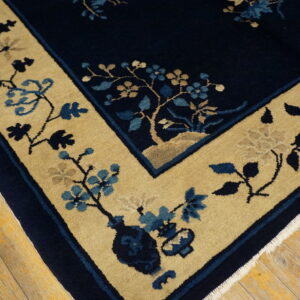 Navy blue and tan rug with a detailed floral border rests on distressed hardwood floors.