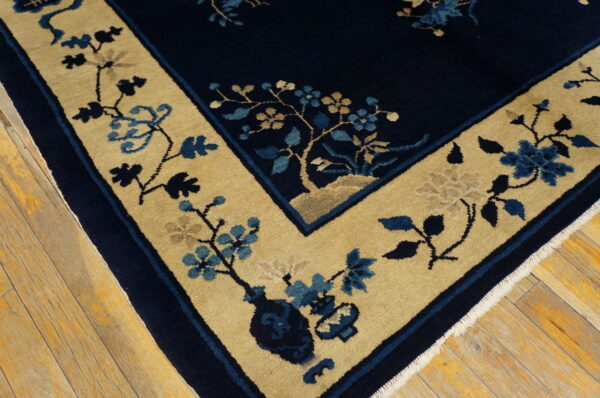 Navy blue and tan rug with a detailed floral border rests on distressed hardwood floors.