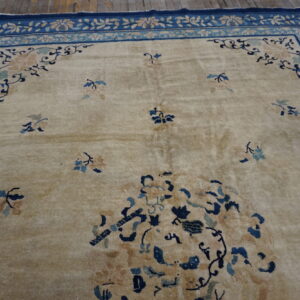 Low-pile beige rug with dark blue floral borders and accents rests on rustic wooden floorboards.