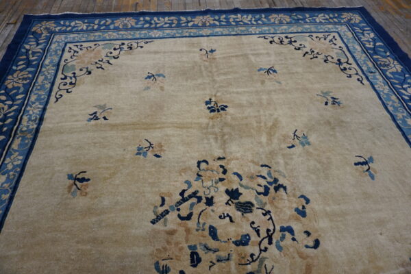 Low-pile beige rug with dark blue floral borders and accents rests on rustic wooden floorboards.