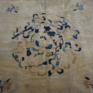 Plush tan rug featuring a stylized floral medallion design in dark blue and muted peach accents.
