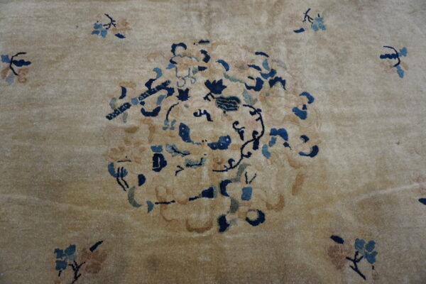Plush tan rug featuring a stylized floral medallion design in dark blue and muted peach accents.