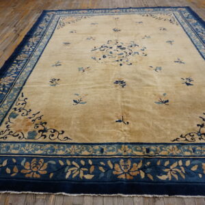 Gold rug with scattered blue motifs and a wide, complex navy and teal floral border on wood.