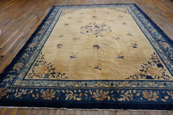 Gold rug with scattered blue motifs and a wide, complex navy and teal floral border on wood.
