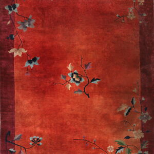 A rust-red rug features a maroon border and stylized flowering vine motifs in muted blue, taupe, and green.
