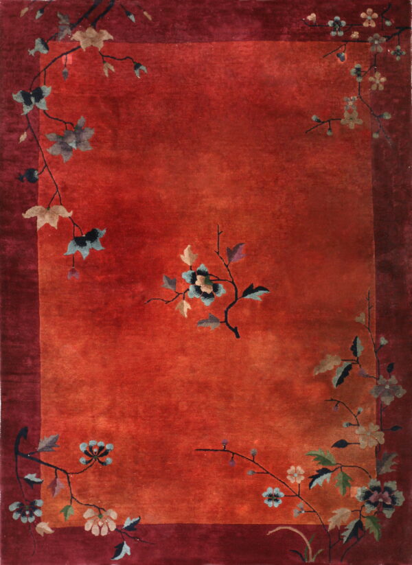 A rust-red rug features a maroon border and stylized flowering vine motifs in muted blue, taupe, and green.