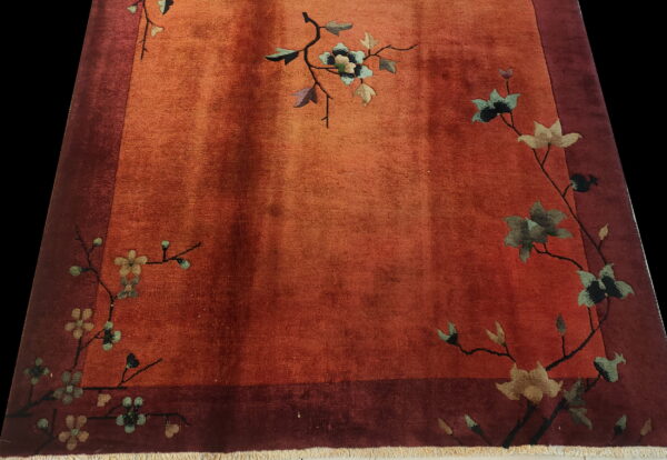 Orange low-pile rug with a dark border and sparse teal and beige floral vine patterns.