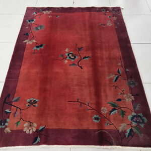 Low pile red rug with flowering branches and a wide maroon border on a bright white tiled floor.