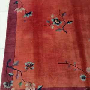 Terracotta and burgundy rug with a sparse floral vine pattern sits on white flooring, showing fringe.