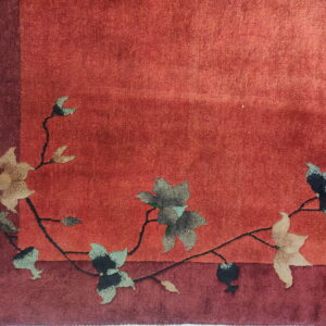 Textured red rug with a darker border showcases a pattern of flowing black vines and muted floral elements.