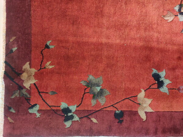 Textured red rug with a darker border showcases a pattern of flowing black vines and muted floral elements.