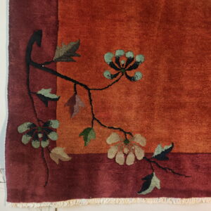 Rust rug corner detail showing a maroon border and a floral vine pattern with teal and beige blossoms.