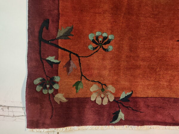 Rust rug corner detail showing a maroon border and a floral vine pattern with teal and beige blossoms.