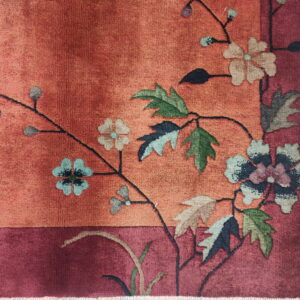 Detailed view of a burnt orange rug with a deep red border and colorful flowering vine motif.