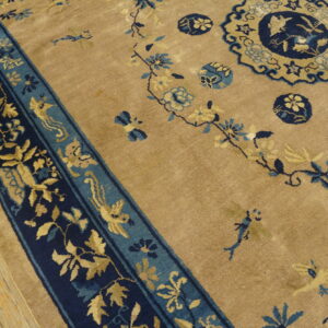 Tan rug with navy border and golden botanical designs, including birds and medallions, resting on wood.