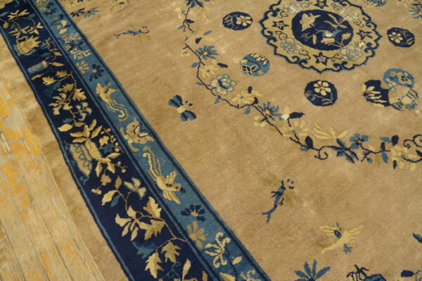 Tan rug with navy border and golden botanical designs, including birds and medallions, resting on wood.