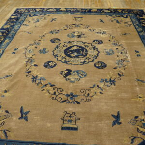 Tan area rug with an elaborate blue medallion pattern, navy border, resting on worn wood flooring.