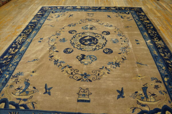 Tan area rug with an elaborate blue medallion pattern, navy border, resting on worn wood flooring.