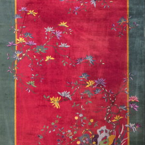 A deep red rug with a teal border and scattered flowering vines in yellow, purple, and gray.