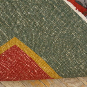 A rug is folded, showing its green, woven back and multicolored floral pile on distressed wooden flooring.