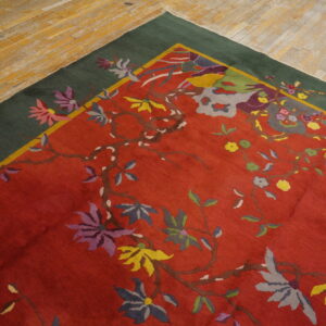 A red rug with a winding multi-colored floral vine pattern and dark green border rests on wood floors.