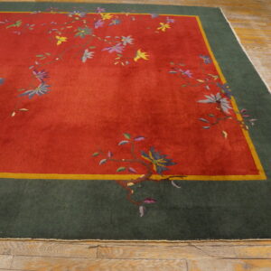 A vibrant red rug with multicolored flowers and a green border rests on worn light hardwood flooring.