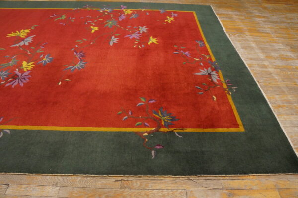 A vibrant red rug with multicolored flowers and a green border rests on worn light hardwood flooring.