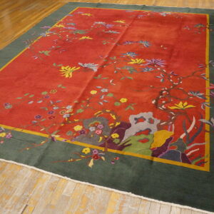Red and dark green rug with a multicolored botanical motif laid on distressed wooden plank flooring.