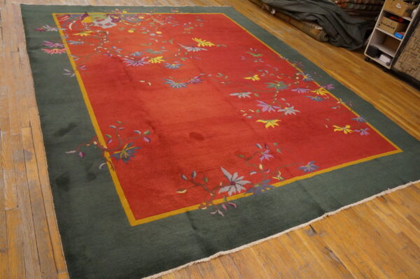 Red field rug with multicolored floral vines, a yellow accent stripe, and a wide dark green border on wood floors.