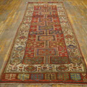 Red and blue geometric runner rug displayed on worn, wide plank hardwood flooring.